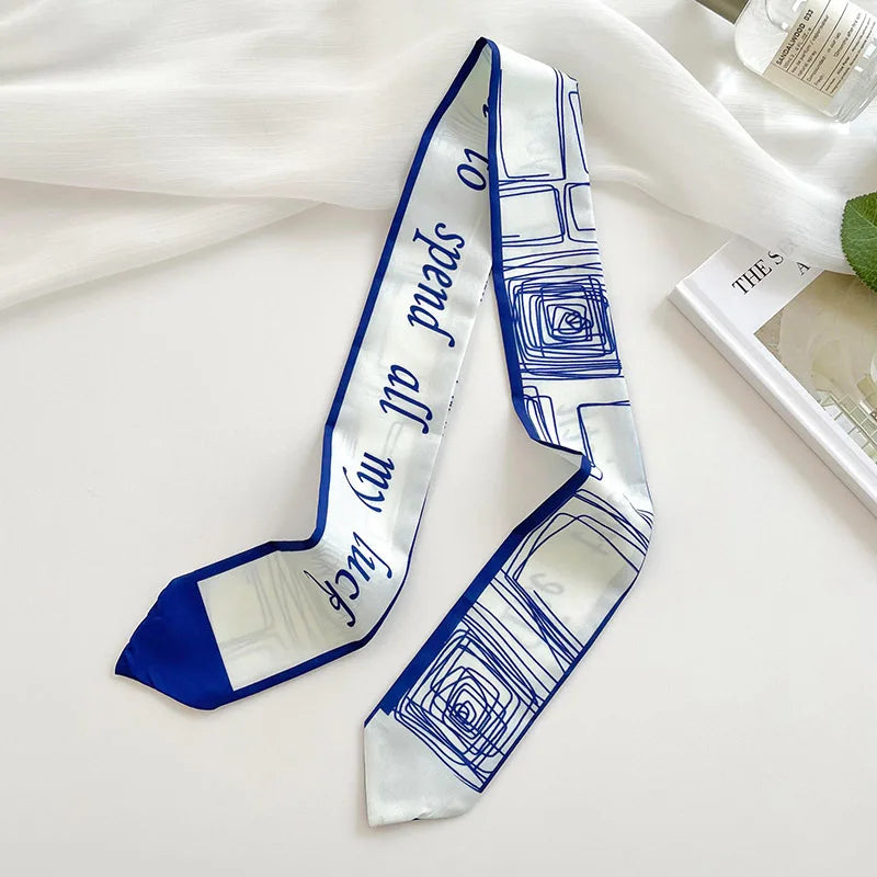 Foulard de cheveux en soie blanc et bleu avec motif géométrique répétitif, exposé sur une surface blanche.