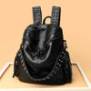 Sac à dos en cuir souple noir rivetée de luxe, exposé sur une surface en bois clair.