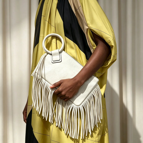 A woman holds a white fringed clutch bag with tassel detail against a yellow and black striped dress.