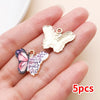A hand holds a set of five gold-toned butterfly enamel charms.