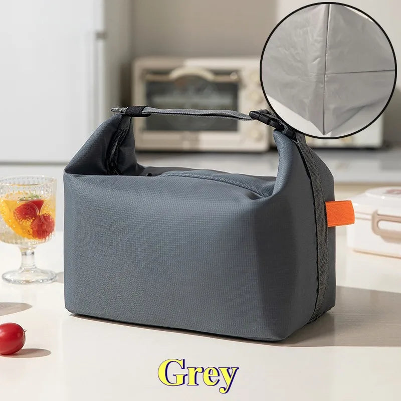 Une trousse à lunch isotherme grise est montrée à côté d'une loupe et d'une pomme rouge sur une surface blanche.