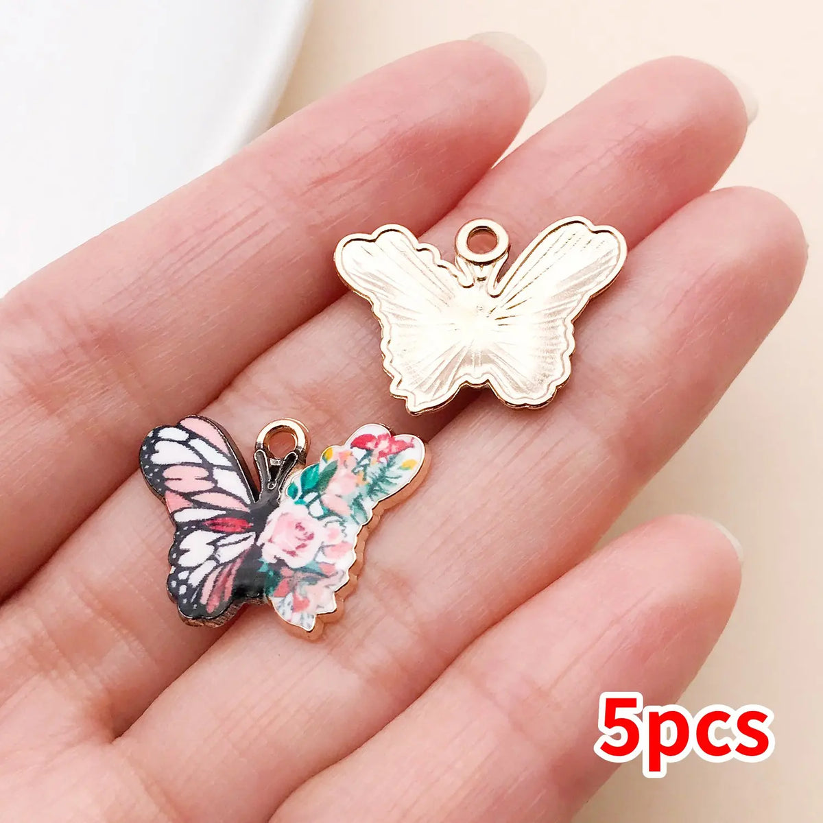 A hand holds a set of five gold-toned butterfly enamel charms.
