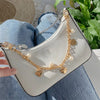 Helles beigees Crossbody-Handtasche mit goldfarbenem Kettchen aus Perlen und Herzen, gehalten von einer Hand auf Jeansstoff.
