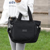 A person holds a black durable nylon tote bag with a secure zipper closure against a blurred outdoor background.