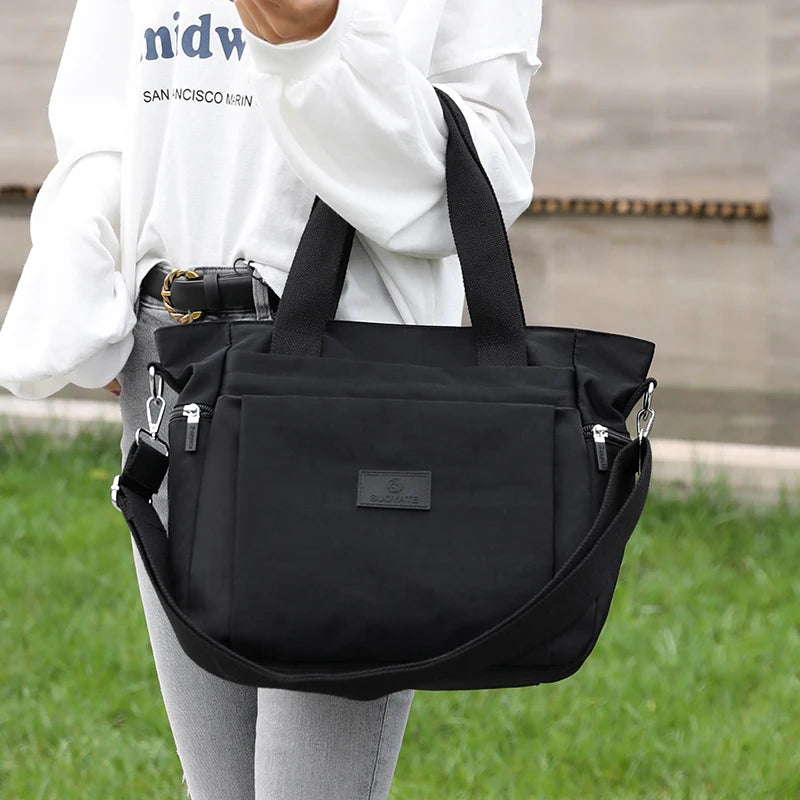 A person holds a black durable nylon tote bag with a secure zipper closure against a blurred outdoor background.