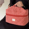 A red and white plaid cosmetic storage bag is held by a person wearing a black garment.