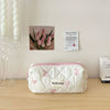 Sac de rangement cosmétique en tissu matelassé blanc avec des imprimés de nœud rose posé sur une surface en bois à côté d'une