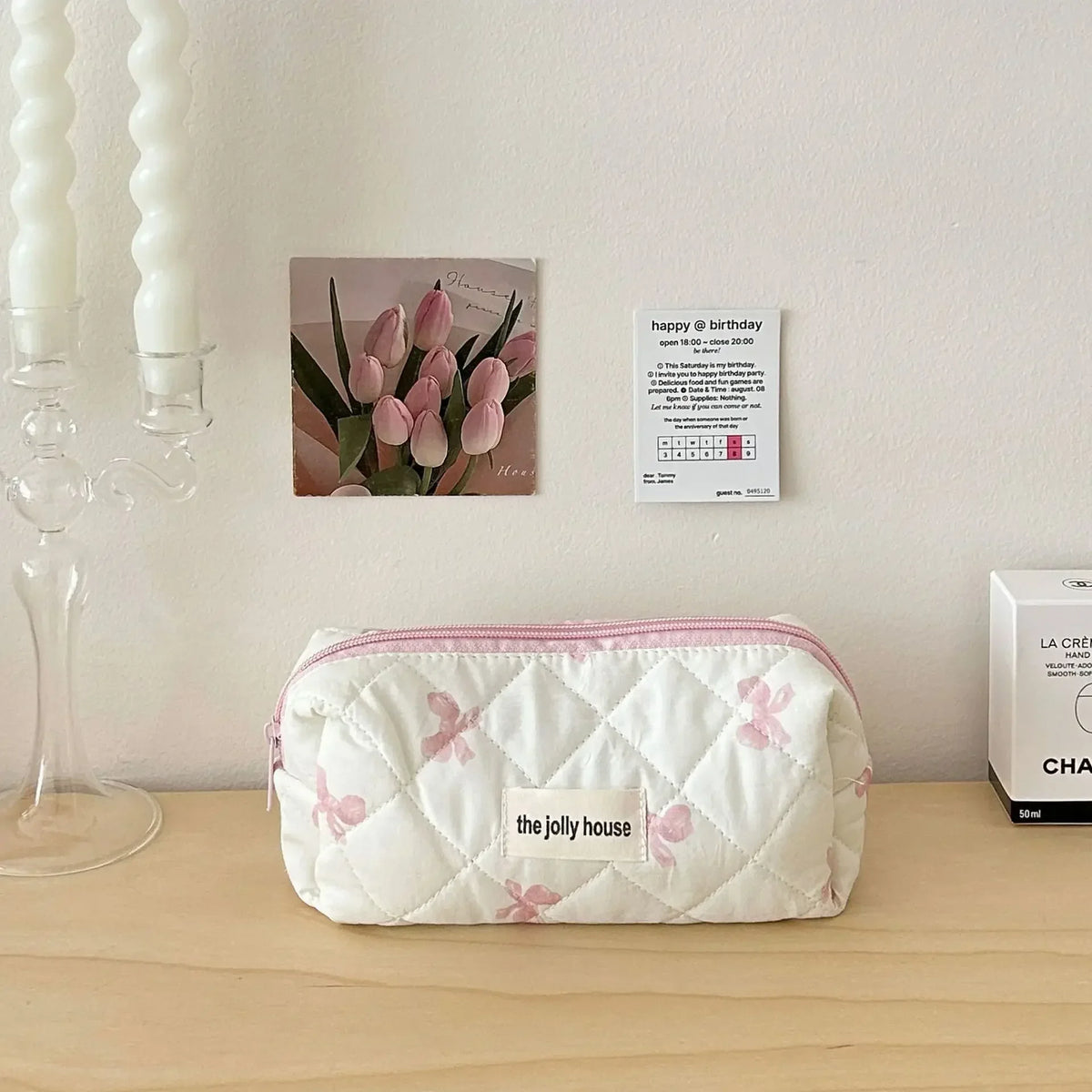 Sac de rangement cosmétique en tissu matelassé blanc avec des imprimés de nœud rose posé sur une surface en bois à côté d'une