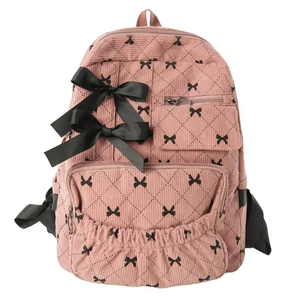 A pink corduroy backpack with a black bow print design and flap pockets.