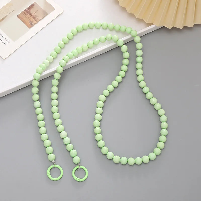 Green acrylic bead cross phone charm necklace laid on a light gray surface.