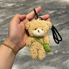 A fluffy tan teddy bear plush toy attached to a black keychain, featuring a green vine and small camera/glasses.