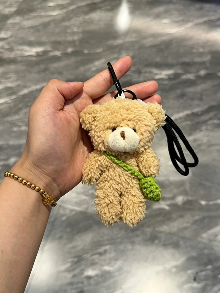 A fluffy tan teddy bear plush toy attached to a black keychain, featuring a green vine and small camera/glasses.