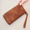 A brown leather tri-fold wallet with a wrist strap and a white leopard print cover is shown in various views.