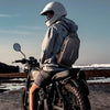 Una persona con casco y sudadera está sentada en una motocicleta con una bolsa cruzada multifuncional.
