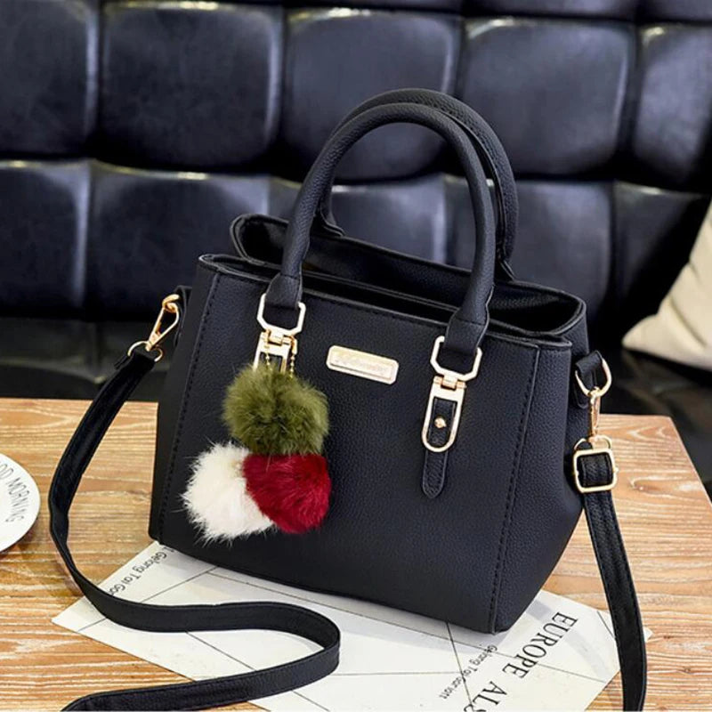 A black vintage PU leather tassel handbag with a fluffy green and white pom-pom decoration resting on a wooden surface.