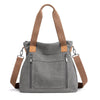A gray canvas tote bag with brown leather straps and pockets shown from the front.
