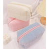 Three stacked cosmetic storage pouches in white, pink, and light blue with zippers.