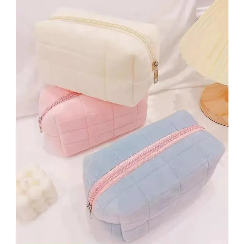Three stacked cosmetic storage pouches in white, pink, and light blue with zippers.