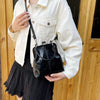 A woman holds a black leather shell handbag with a strap against a light jacket and a black skirt.
