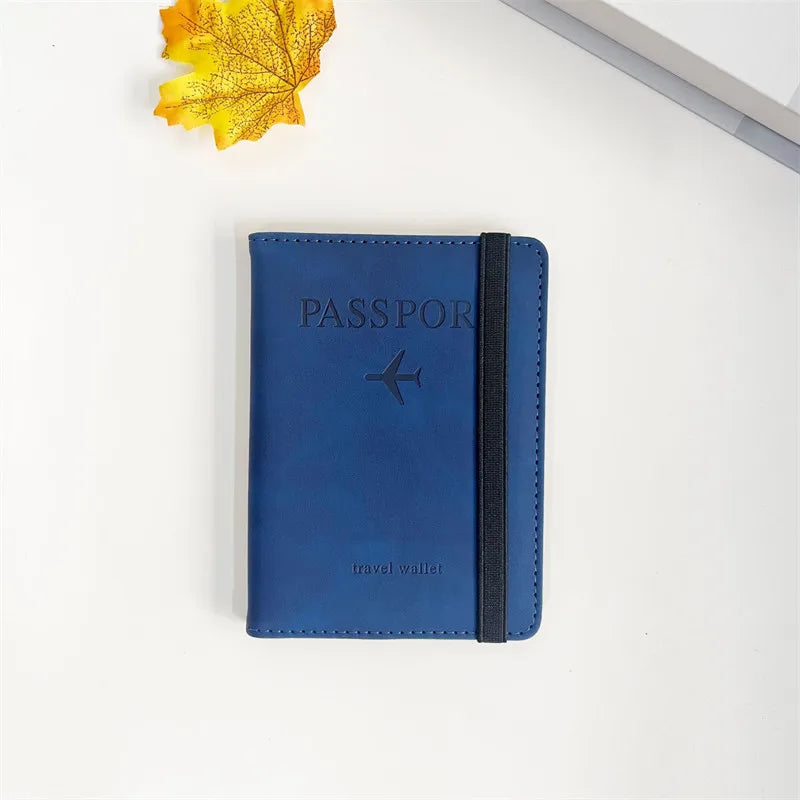 A dark blue passport wallet with a black zipper is shown next to a yellow autumn leaf.