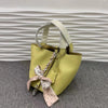 Helles gelbes Leder-Bucket-Bag mit weißem Riemen und rosa Blumenband, vor grauem Hintergrund.