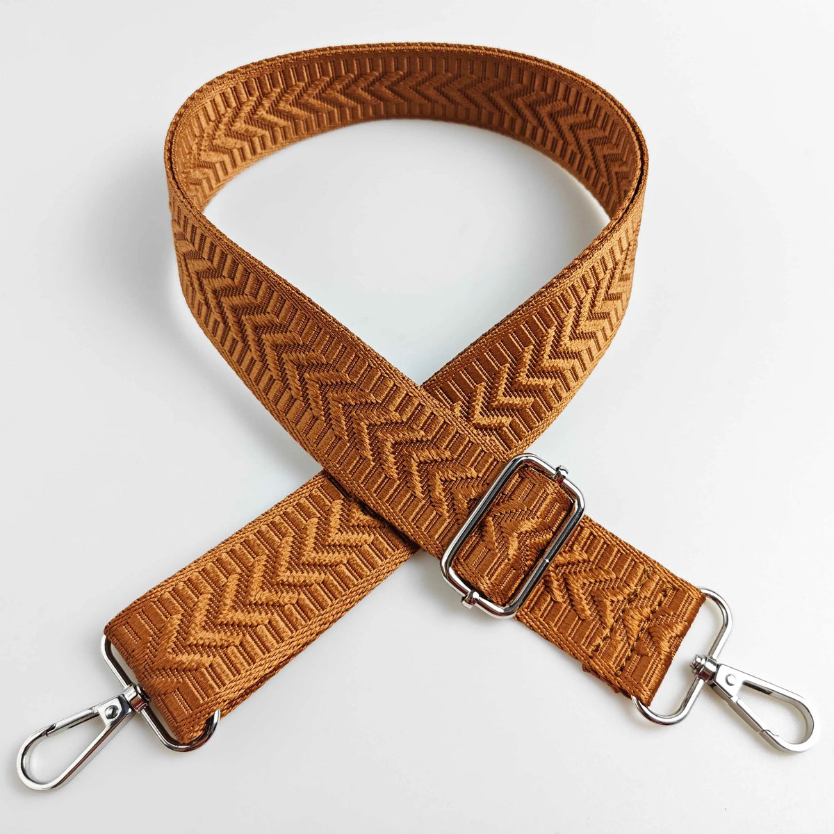 A close-up of a woven brown leather handbag strap featuring an arrow jacquard pattern.