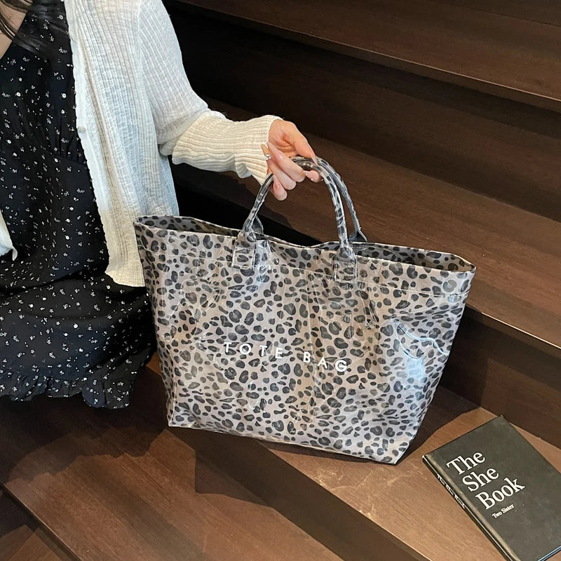 Eine Frau hält eine Leopardenmuster-PVC-Tasche vor einem dunklen Holz Hintergrund.
