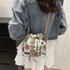 A close-up of a floral drawstring bucket bag with beige leather accents worn on a denim jacket.
