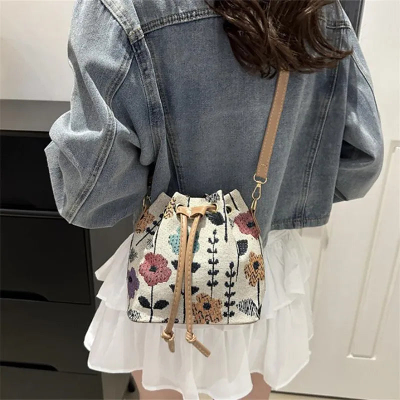 A close-up of a floral drawstring bucket bag with beige leather accents worn on a denim jacket.