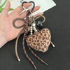 A brown leather and leopard print plush heart pendant keychain is held in a person's hand.