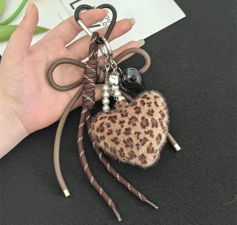 A brown leather and leopard print plush heart pendant keychain is held in a person's hand.