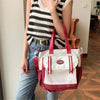 Eine Frau hält eine weiße und rosa Nylon-Tasche mit roten Riemen vor einem hellen Hintergrund.