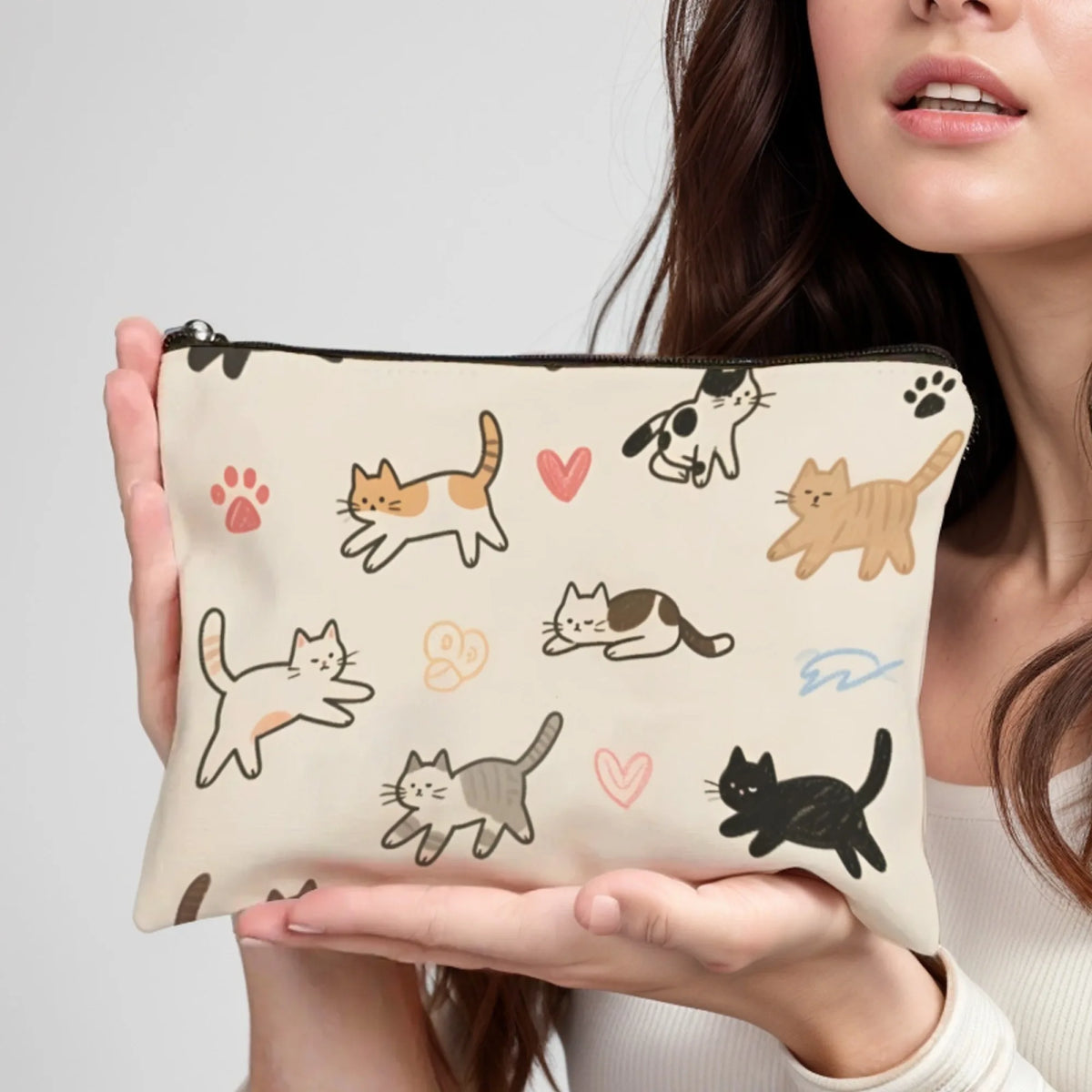 A hand holds a beige cartoon cat cosmetic pouch featuring various cat illustrations.