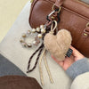A brown leather heart pendant keychain with long tassels is displayed against a light background.
