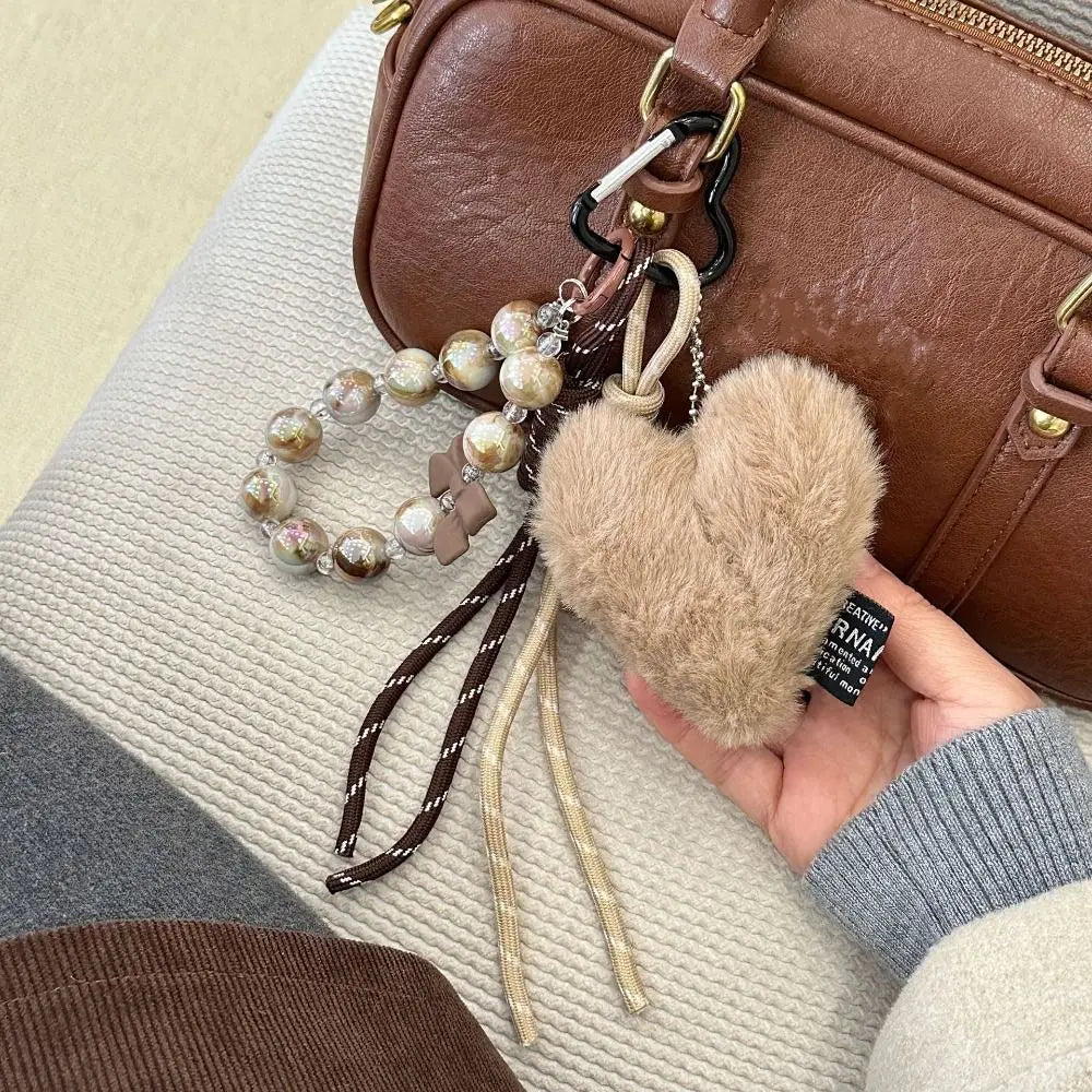 A brown leather heart pendant keychain with long tassels is displayed against a light background.
