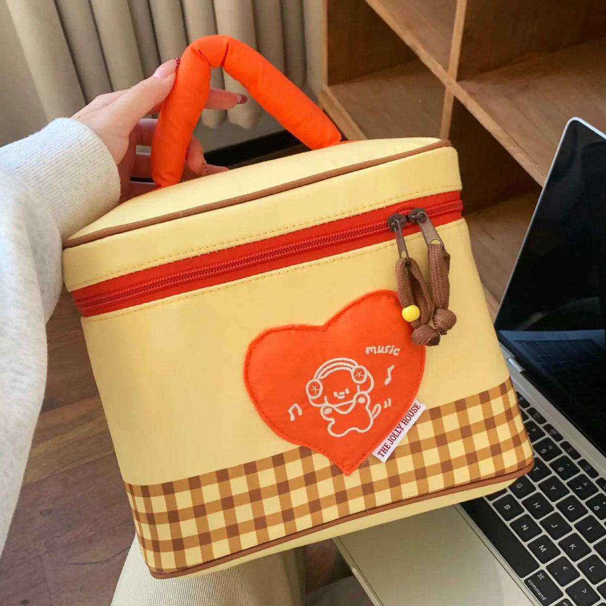 A yellow insulated lunch bag with an orange handle and a heart-shaped patch featuring a cartoon character.