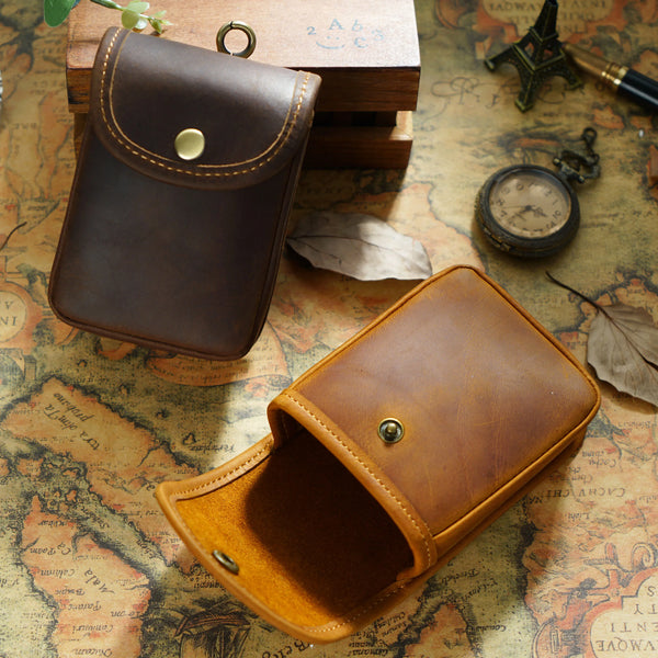 Bolsa de cintura de cuero marrón multifuncional abierta sobre un mapa texturizado junto a una caja de madera y una cámara vin