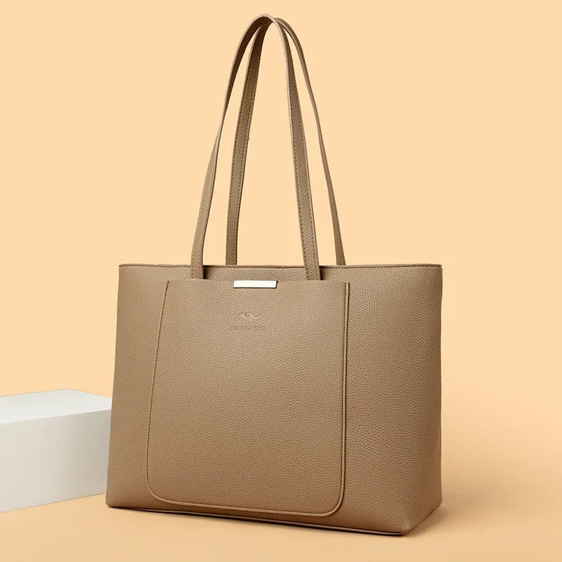 A tan leather shoulder bag with long handles is shown against a light beige background.