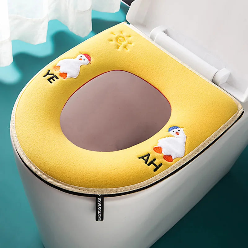 A yellow plush waterproof toilet seat cover with embroidered faces of a bird and a fish.
