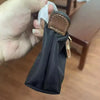 A hand holds a black nylon crossbody bag with a brown leather detail and a white drawstring.