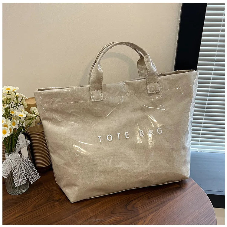 A light beige transparent waterproof PVC tote bag resting on a wooden surface.
