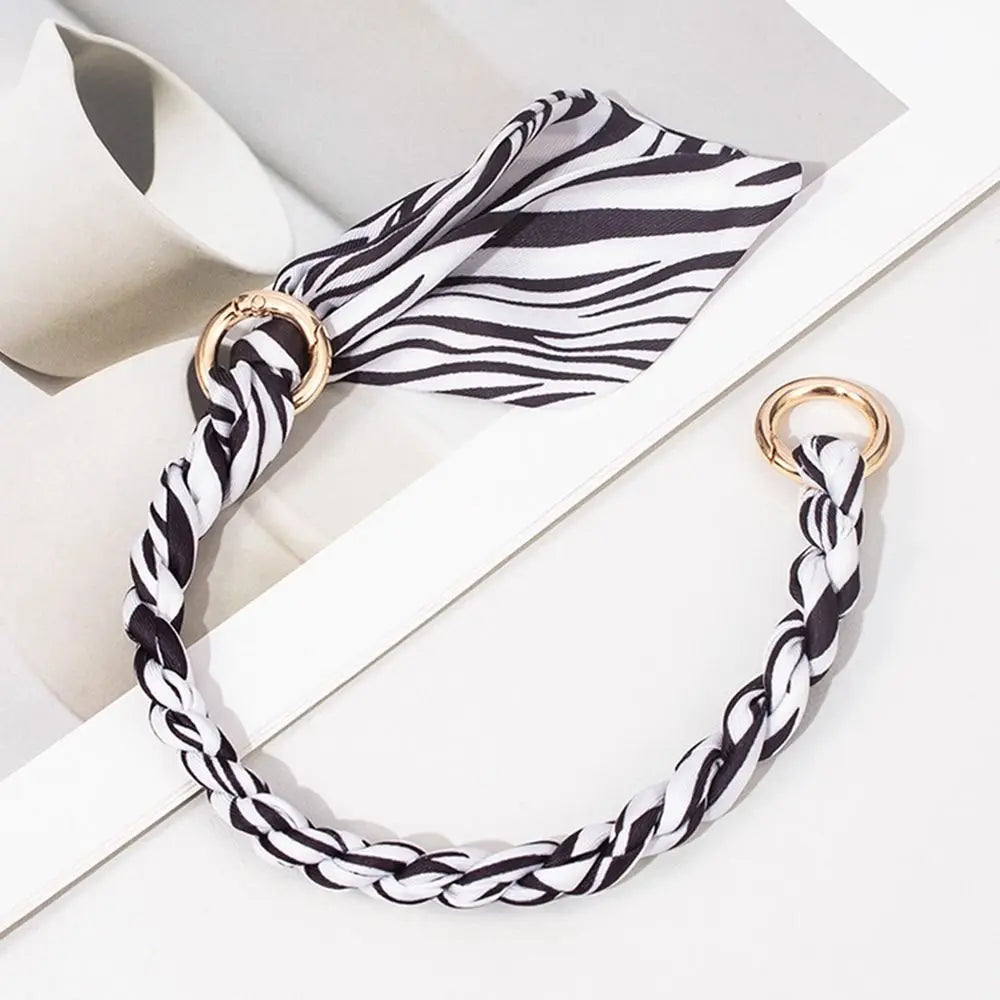 Schlagschleiftasche mit schwarz-weißem Zebra-Muster aus Seide und Kette vor weißem Hintergrund