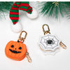 Cartera de monedas en forma de calabaza junto a un dije de telaraña y follaje navideño.