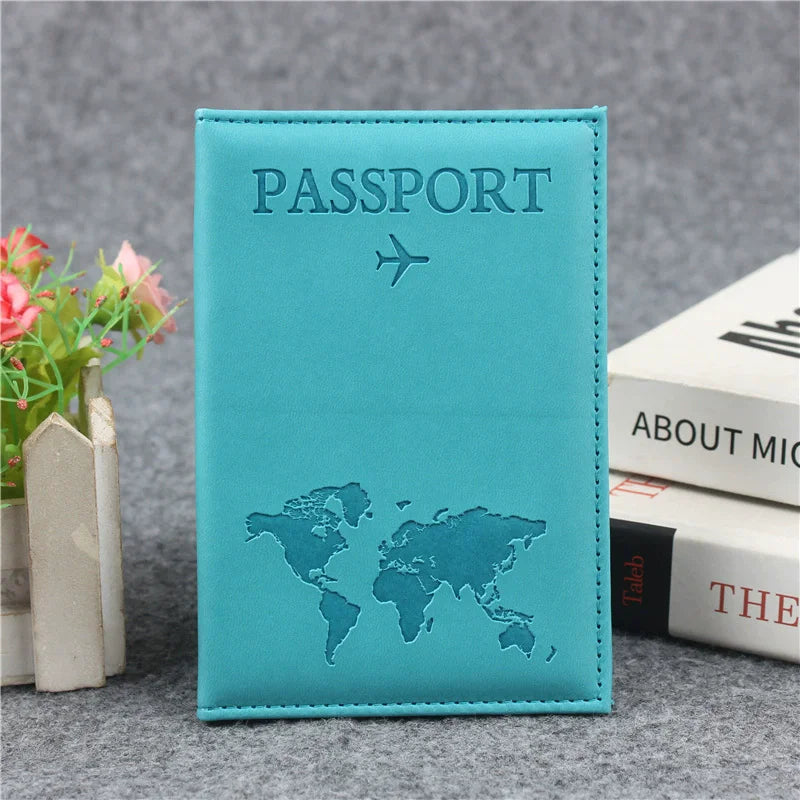 Housse de passeport en cuir PU bleu sarcelle avec une icône d'avion argentée et une carte du monde sur une surface grise.
