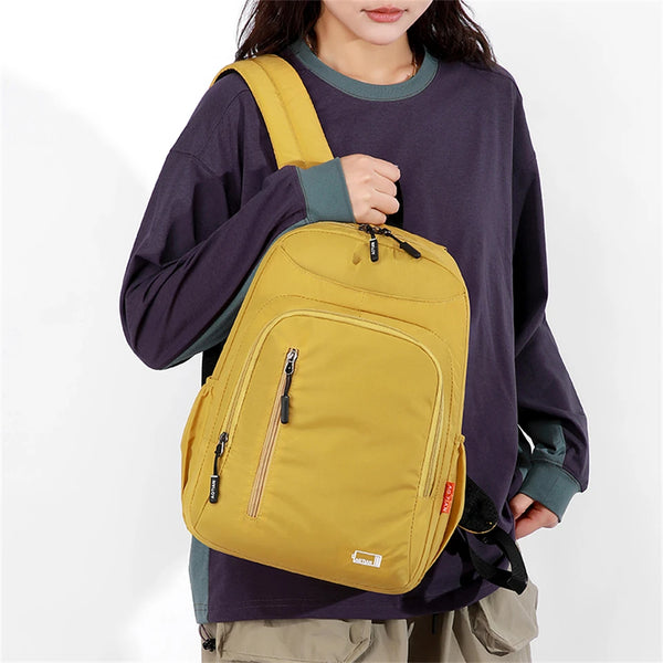 A woman wearing a purple long-sleeved shirt carries a yellow fashion commuter daypack on her shoulder.