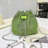 Bolso cruz de cordón brillante con pedrería verde lima y cadena plateada sobre una superficie blanca.