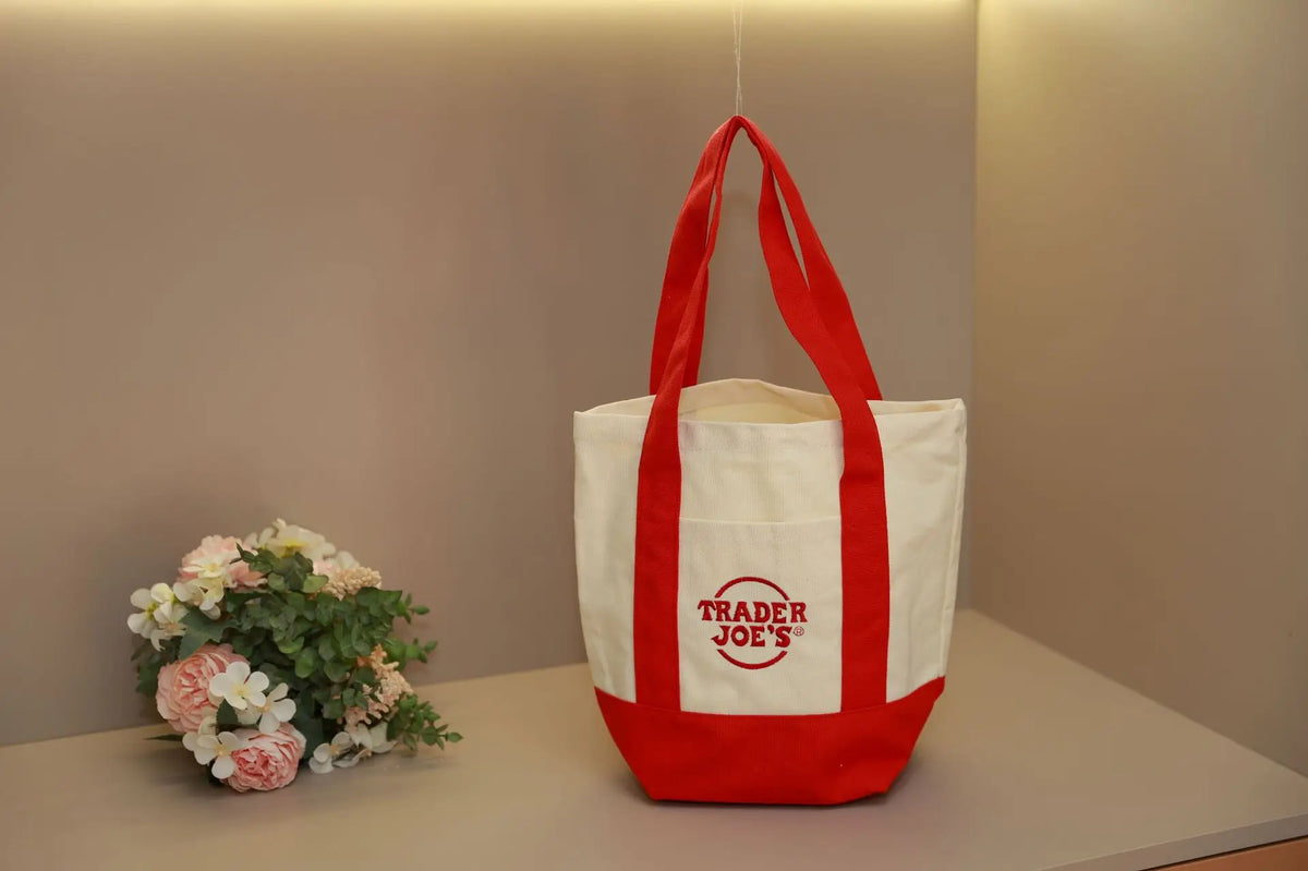 A white canvas bag with red handles and trim is displayed on a light surface.