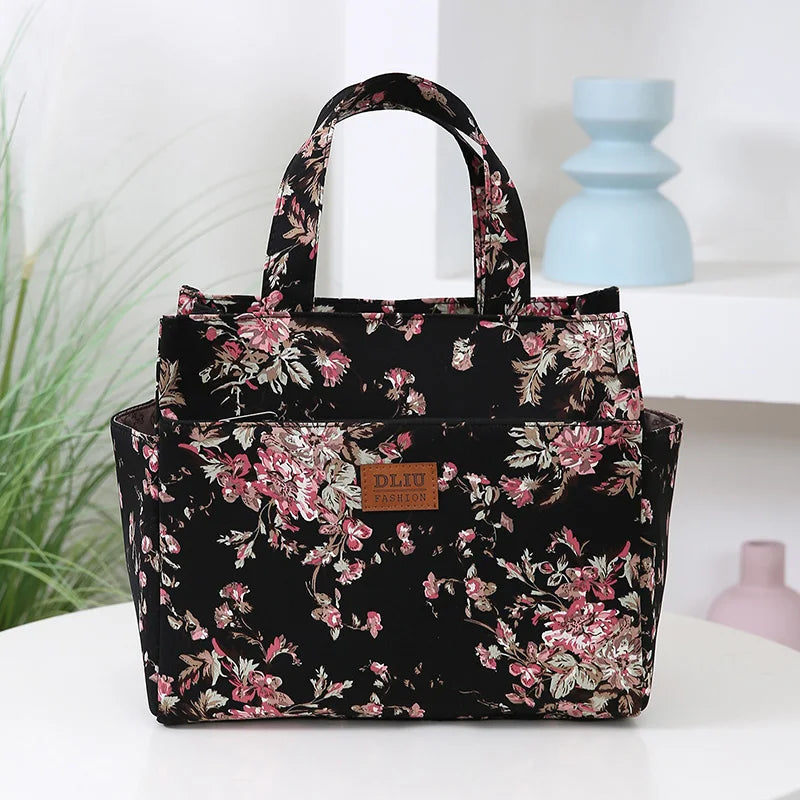 A black cloth tote bag with a floral pattern and handles is displayed on a white surface.