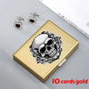 A gold card holder featuring a detailed skull design surrounded by floral elements, with small silver earrings nearby.