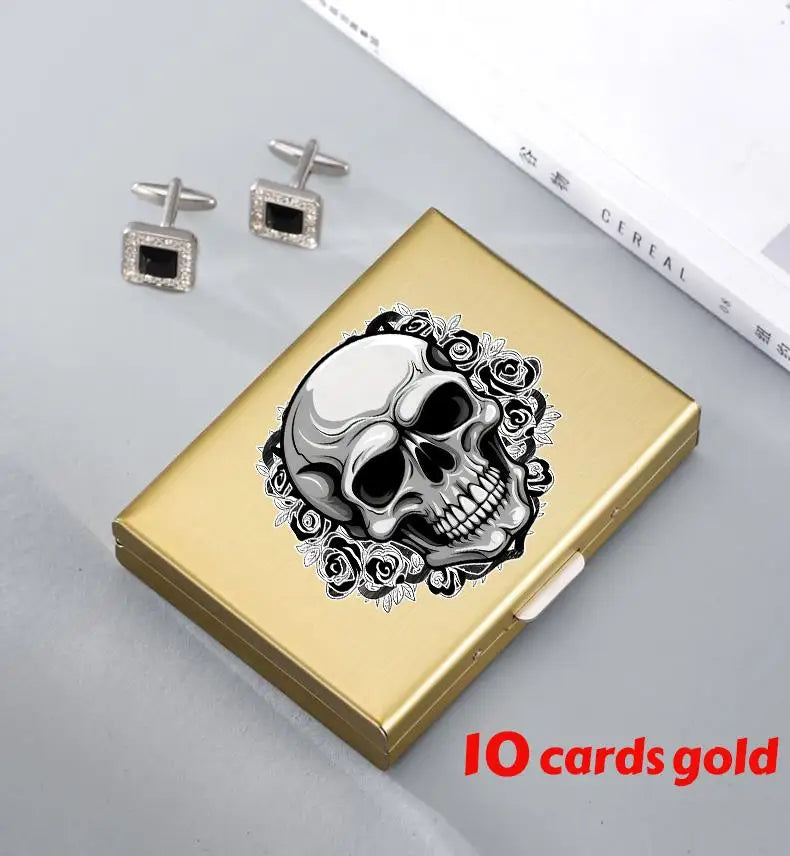 A gold card holder featuring a detailed skull design surrounded by floral elements, with small silver earrings nearby.